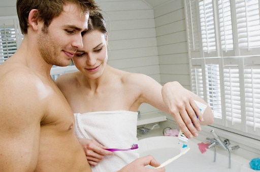 Couple in a bathroom squeezing toothpaste onto toothbrushes